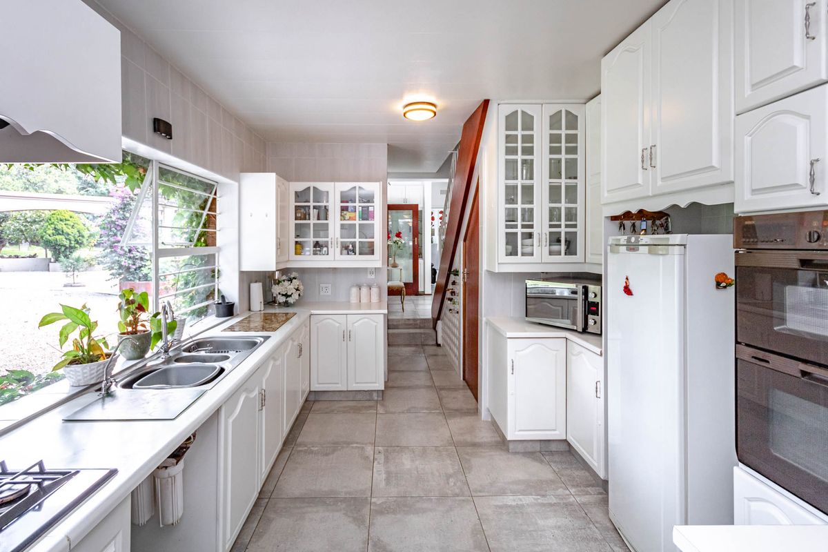 A functional kitchen featuring white cabinetry, tiled flooring, double sink, and built-in oven, with a view through to the adjacent living area.