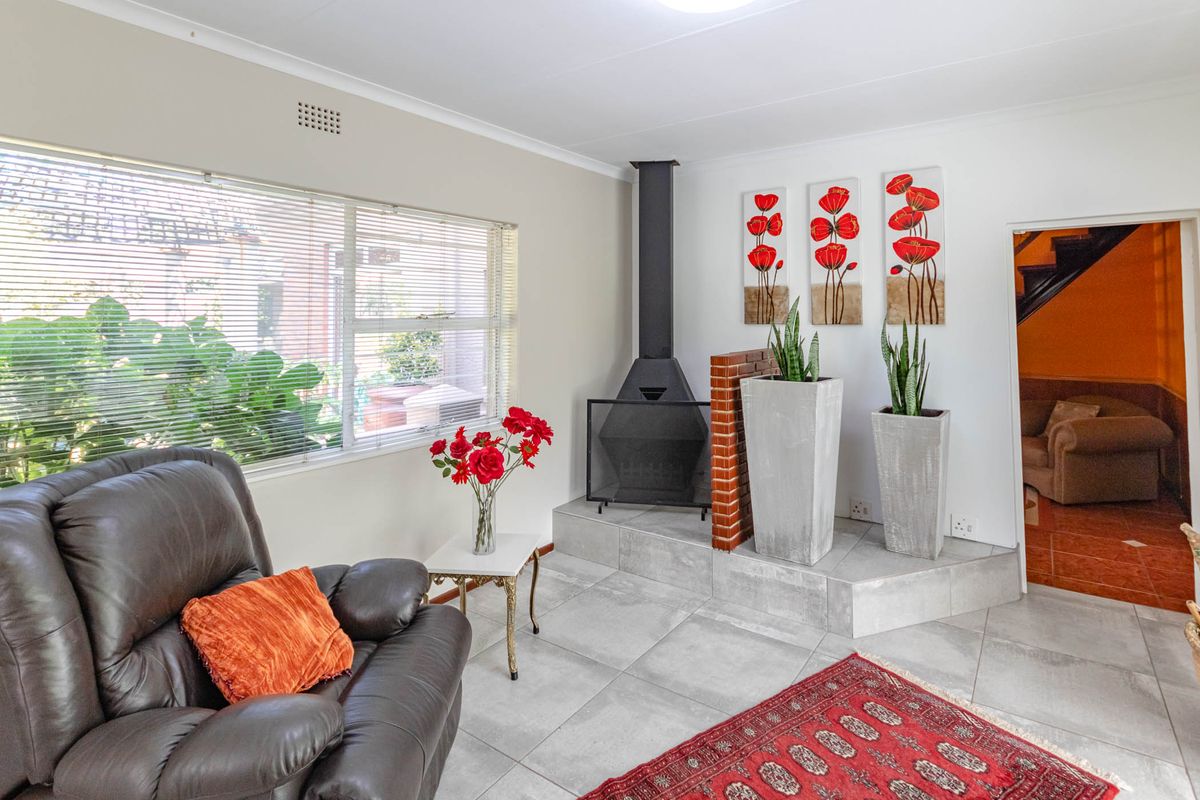 A living room featuring a built-in metal fireplace on a raised tiled hearth, large windows, and neutral floor tiling.