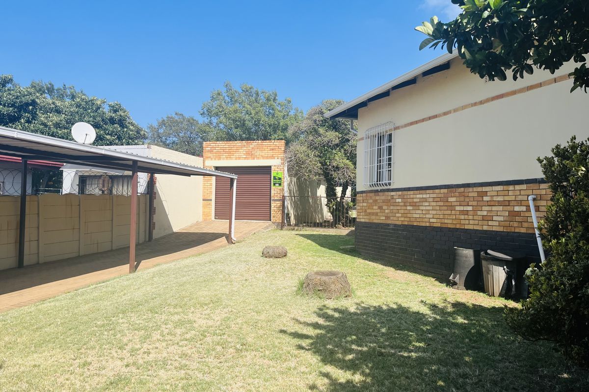 A view of the rear garden area featuring a paved carport, a brick garage, and a lawned yard adjacent to the main house structure.