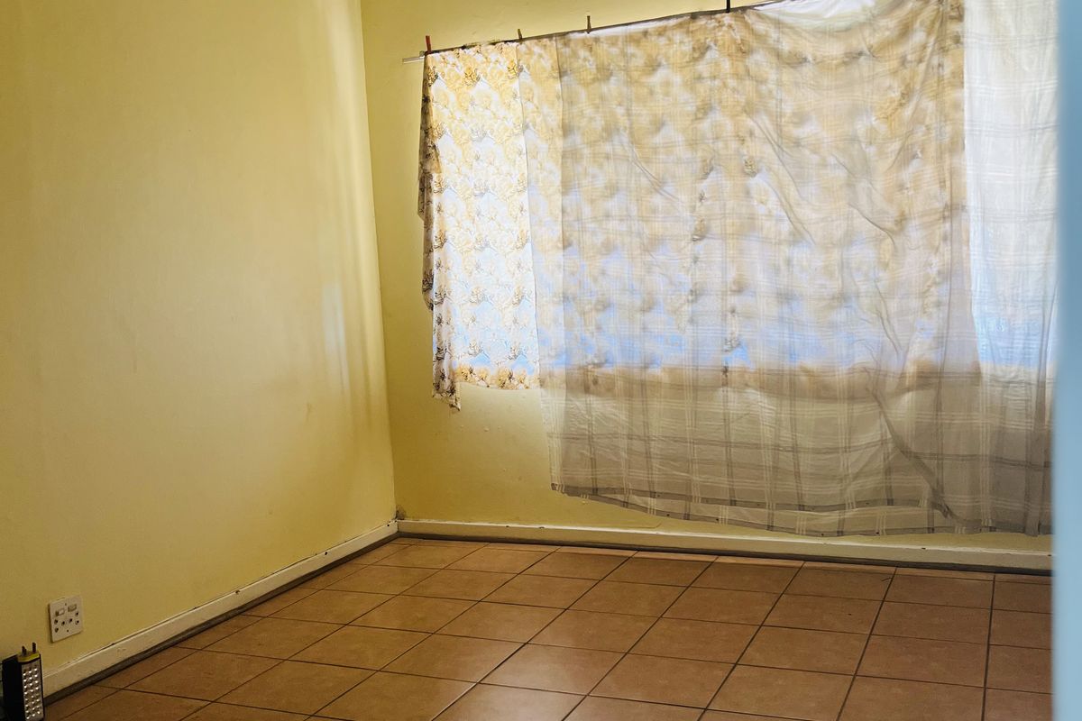 A vacant bedroom featuring tiled flooring, a ceiling fan, and large windows with existing curtain fixtures.
