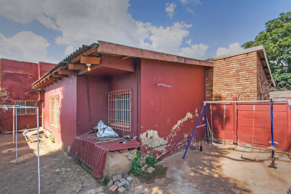 Rear exterior view of the property featuring a red painted facade, security bars on windows, and a paved outdoor area with perimeter walling.