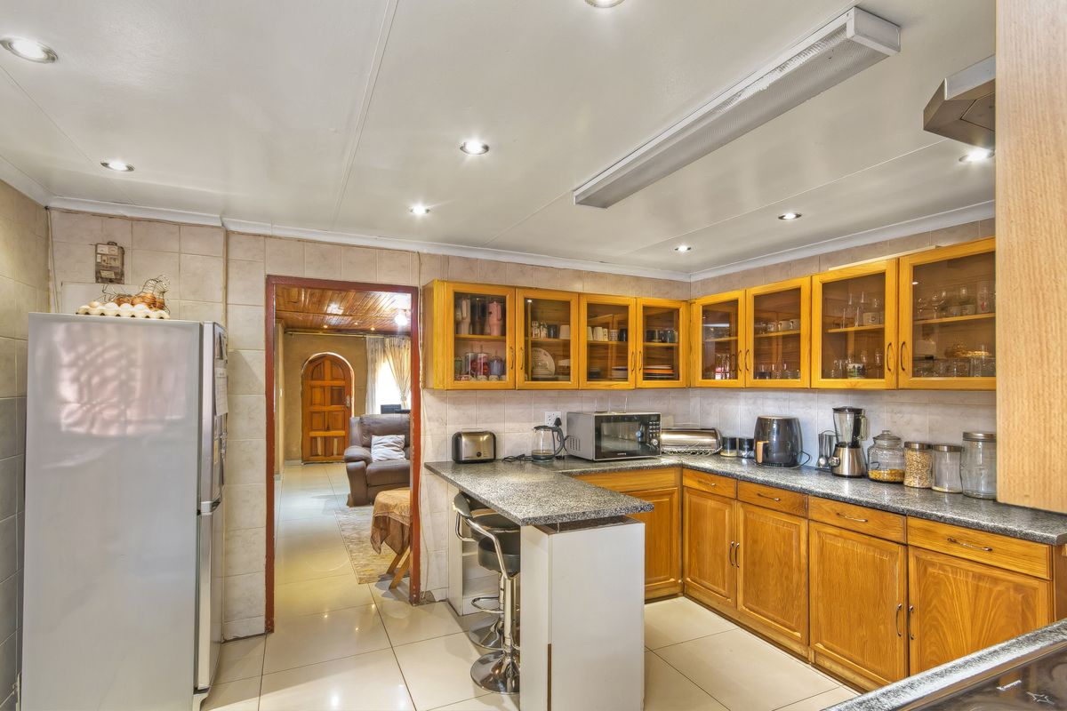 A functional kitchen featuring wooden cabinetry, granite countertops, tiled flooring, and recessed lighting, with an open doorway leading to an adjacent living area.