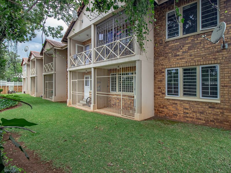 Rear view of the apartment complex featuring face brick exterior, ground floor patios with security gates, and upper-level balconies.