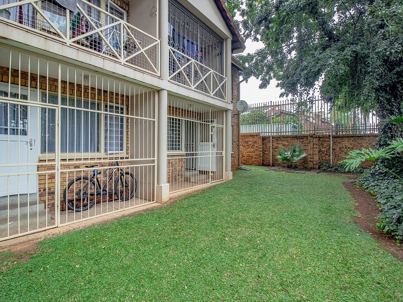 Rear view of the apartment building featuring a private garden, lawn area, and secure balcony with metal security gates and bars.