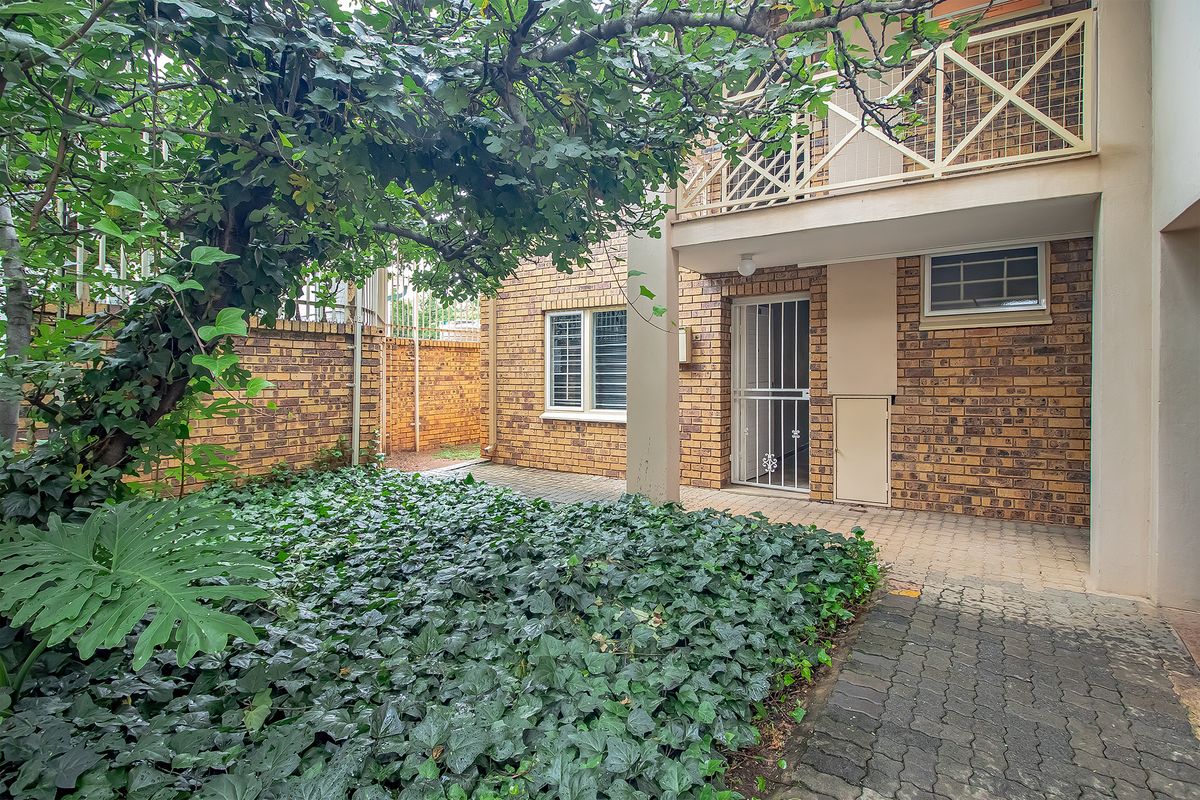 A private rear courtyard featuring a paved patio area, established garden, and access to a balcony above.