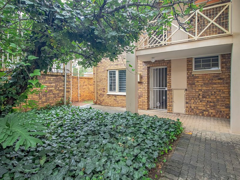 A private rear courtyard featuring a paved patio area, established garden, and access to a balcony above.