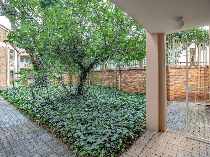 A private rear courtyard featuring paved walkways, established garden beds, and a secure gated entrance under a covered patio area.