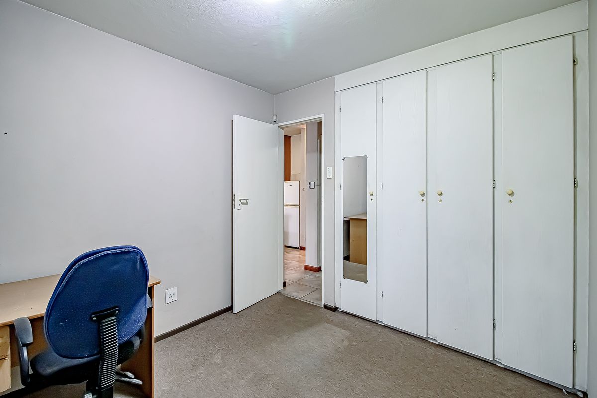 A bedroom featuring built-in cupboards with a mirrored panel and carpeted flooring, offering a functional space with potential for cosmetic updates.