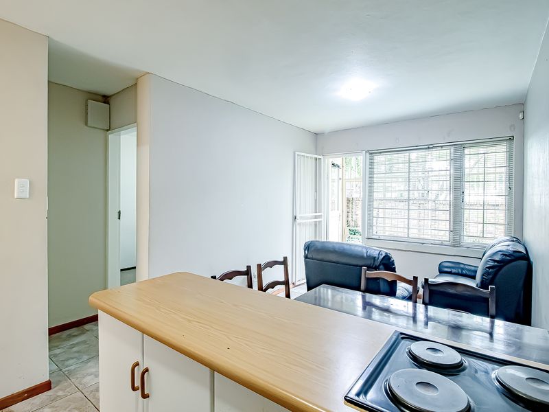 Open plan living and kitchen area featuring a breakfast counter, electric hob, and direct access to an outdoor space through a security gate.
