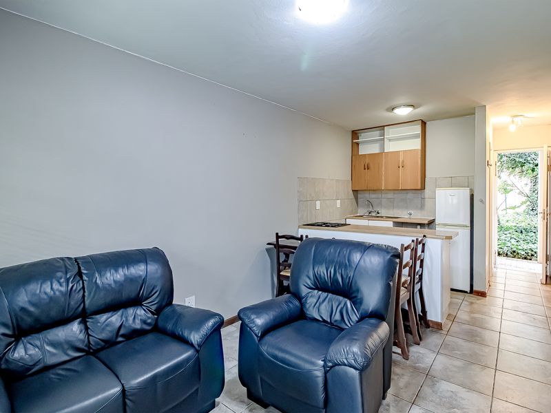 Open plan living area featuring a compact kitchen with built-in cabinetry, tiled flooring, and direct access to an outdoor space.