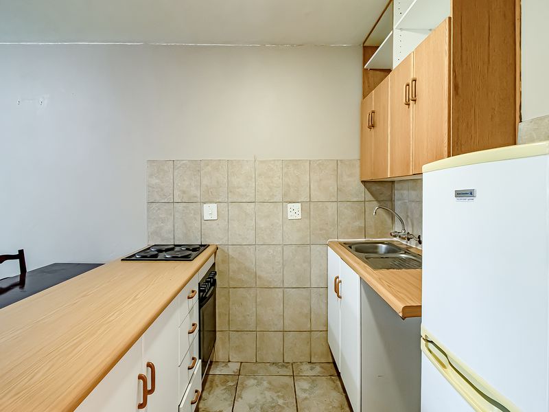 Compact kitchen featuring laminate countertops, built-in cabinetry, an electric hob, oven, and tiled backsplash, offering a functional layout for an apartment.