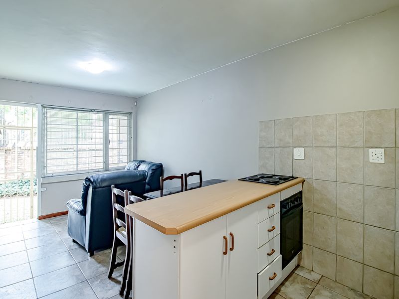 Open plan kitchen and living area featuring tiled floors, built-in cabinetry with oven and hob, and direct access to an outdoor space.