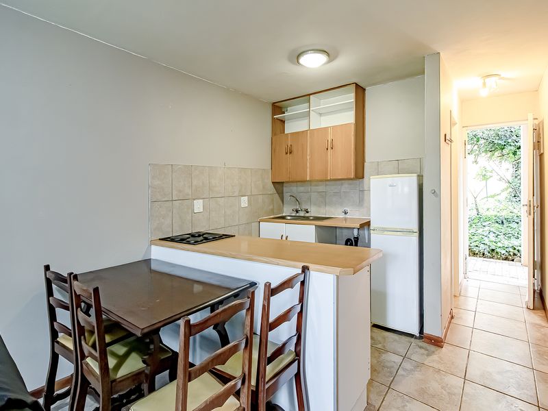 Compact kitchen area featuring built-in cabinetry, a hob, and tiled backsplash, with direct access to an outdoor space.