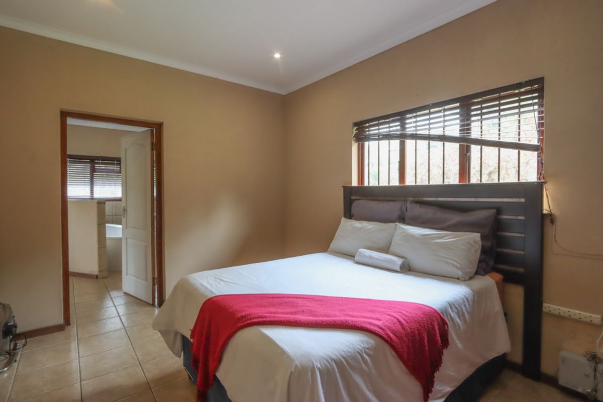 A bedroom featuring tiled flooring, recessed ceiling lighting, and an adjoining bathroom, with a window fitted with security bars and blinds.