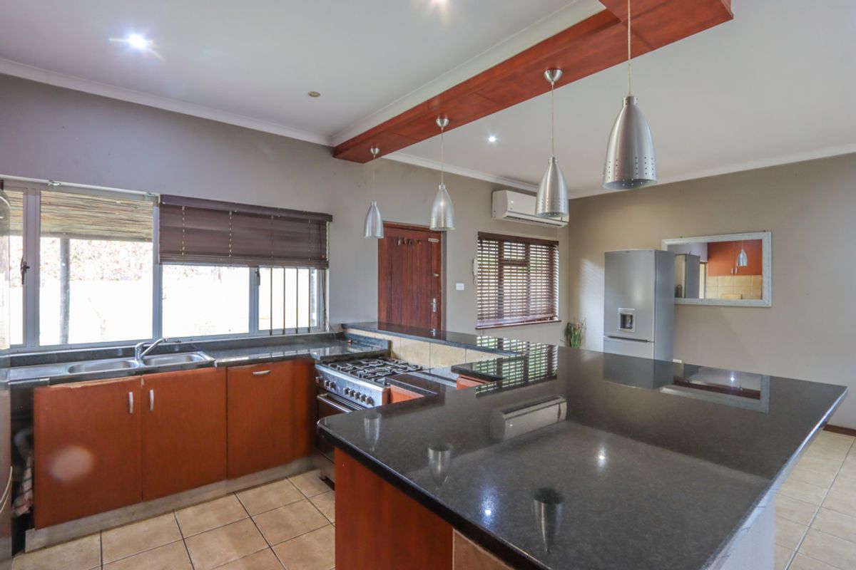 A functional kitchen featuring dark granite countertops, wooden cabinetry, a gas stove, and a breakfast bar island with pendant lighting.