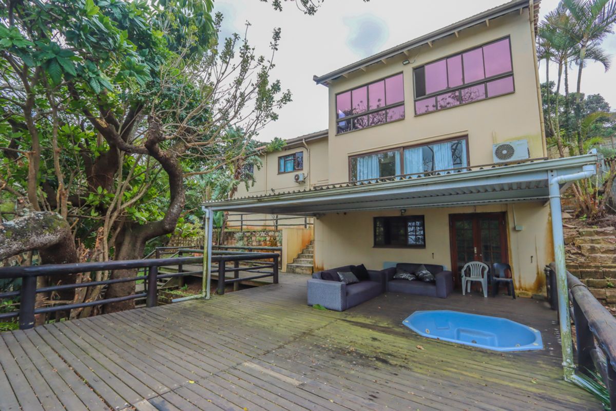 Rear exterior view featuring a multi-level timber deck, covered patio area, and a built-in plunge pool set against a landscaped garden.