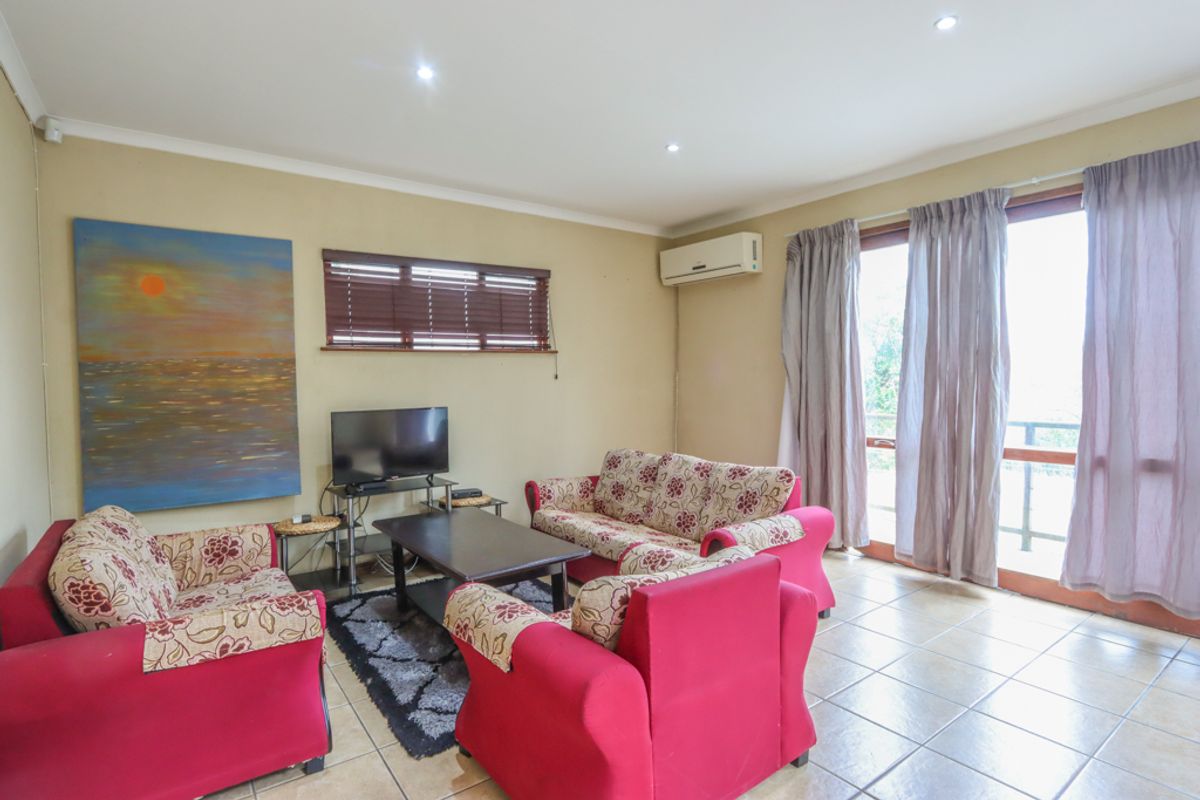 A comfortable living room featuring tiled flooring, recessed ceiling lighting, a wall-mounted air conditioning unit, and sliding glass doors leading to an outdoor area.