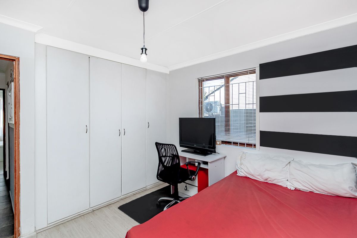 A bedroom featuring built-in cupboards, a window with security bars, and laminate flooring.