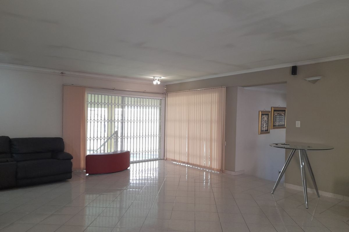Spacious living area featuring tiled flooring, large sliding glass doors with security gates, and vertical blinds, offering a bright and open layout.