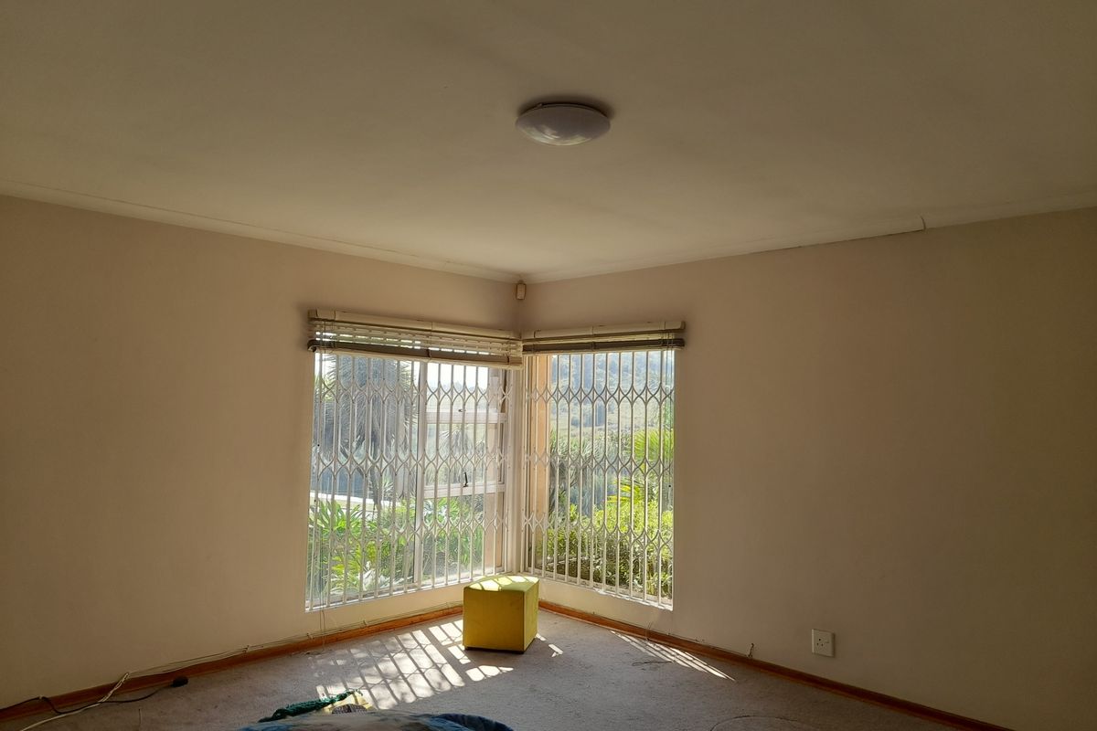 A spacious, empty bedroom featuring corner windows with security bars, neutral walls, and carpeted flooring.