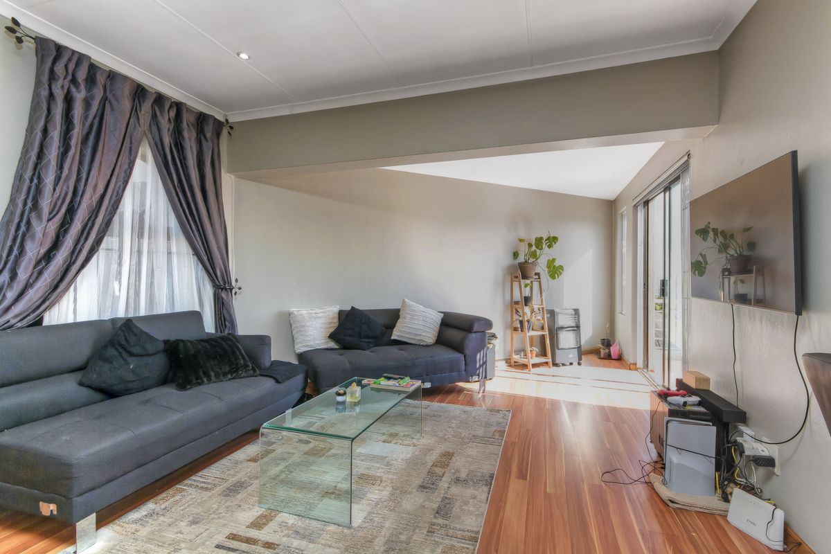 A comfortable living room featuring warm-toned laminate flooring, recessed lighting, and large sliding glass doors that provide access to the outdoor area.
