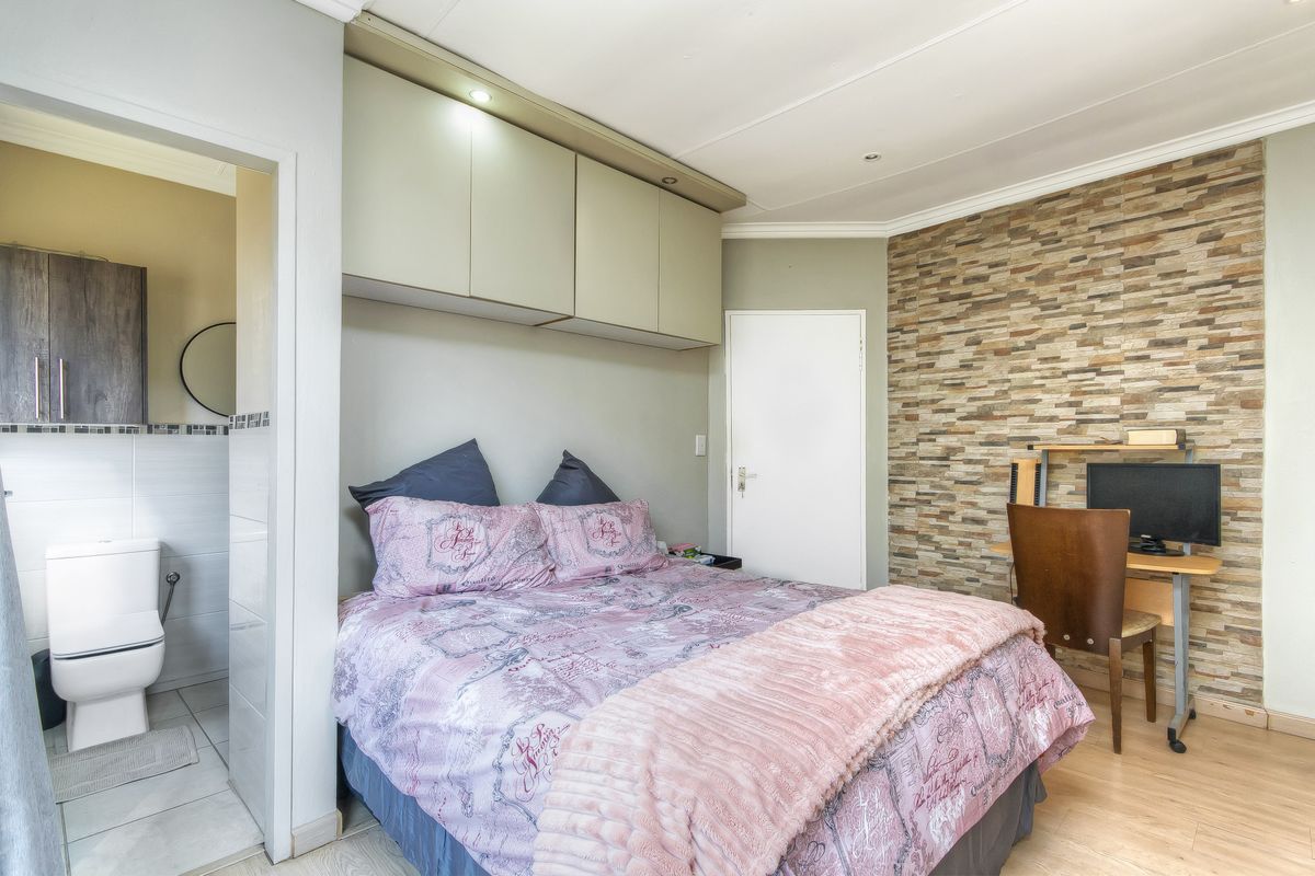 Bedroom featuring built-in overhead cabinetry, a textured stone veneer feature wall, laminate flooring, and direct access to an en-suite bathroom.