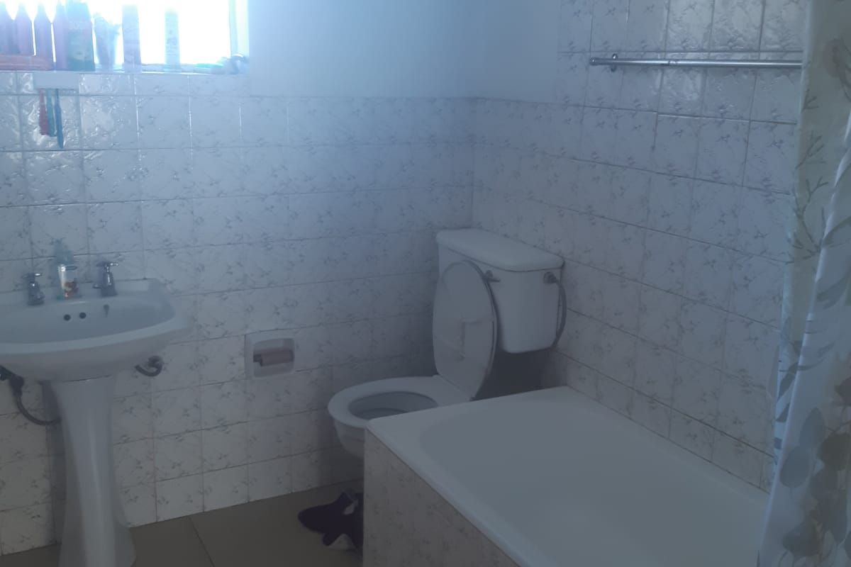 A functional bathroom featuring a pedestal basin, a standard bathtub with shower curtain, and a toilet, finished with dated wall and floor tiling.