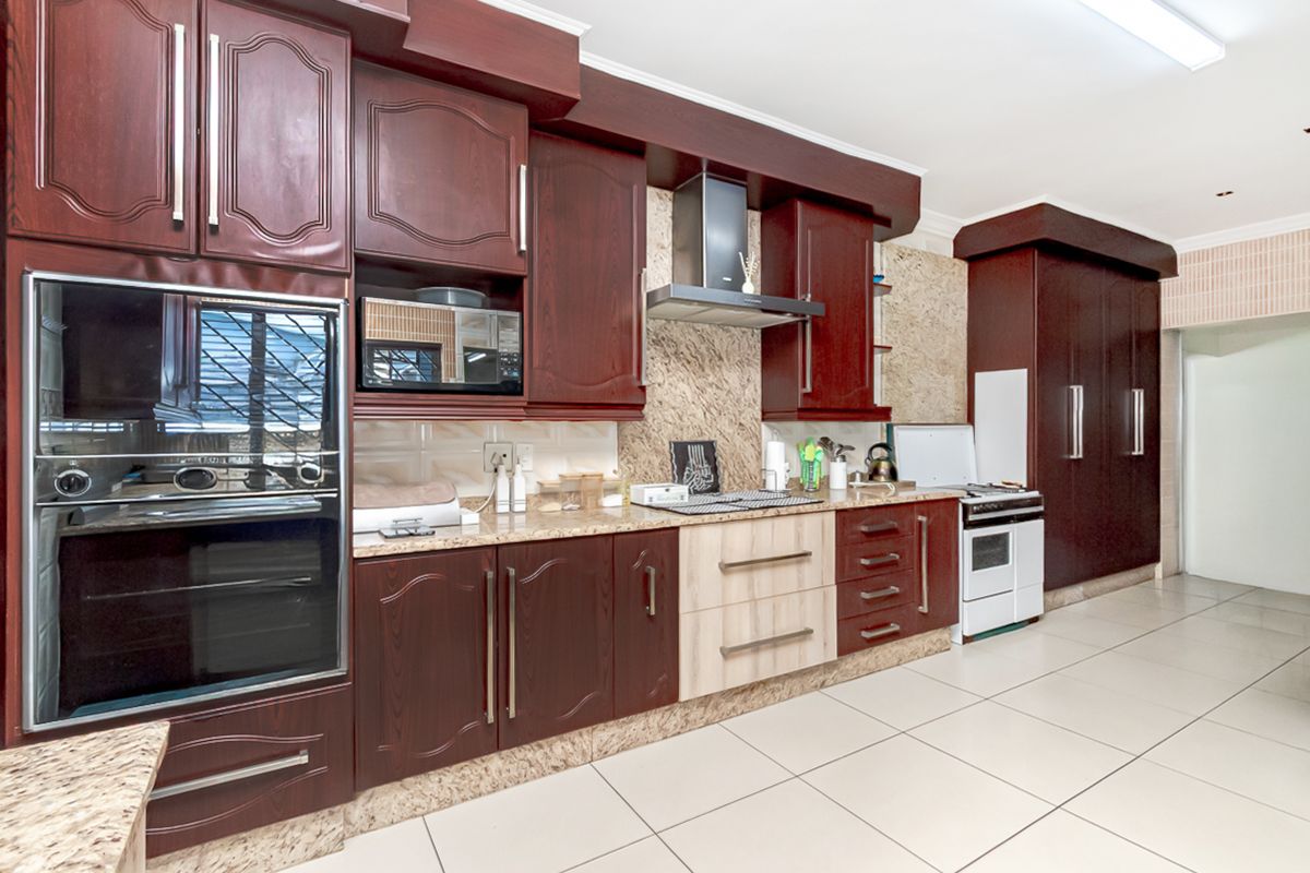 A spacious kitchen featuring dark wood cabinetry, granite countertops, built-in oven, extractor fan, and tiled flooring.
