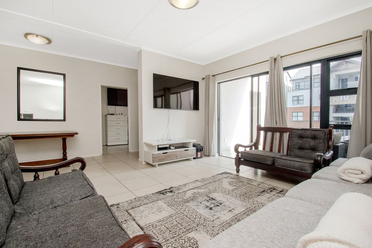 A bright and spacious living room featuring neutral tiled flooring and large sliding glass doors that provide access to an outdoor balcony area.