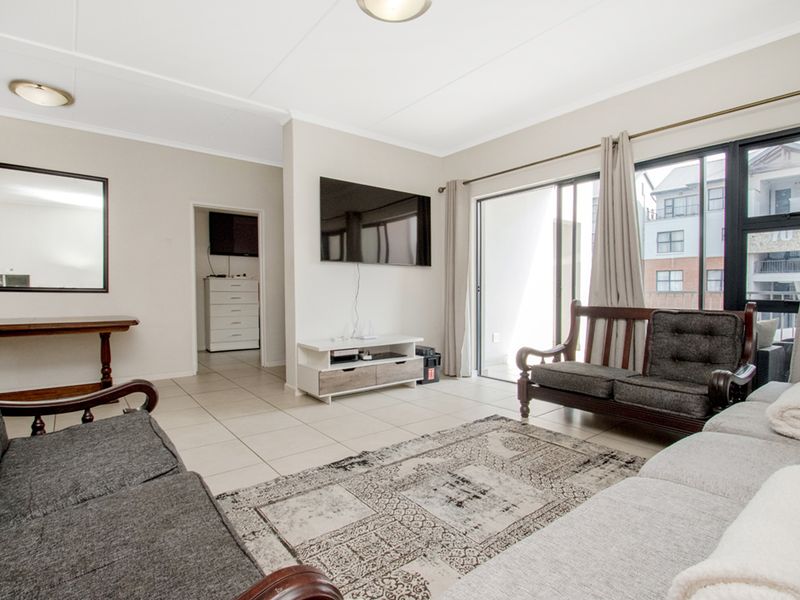 A bright and spacious living room featuring neutral tiled flooring and large sliding glass doors that provide access to an outdoor balcony area.