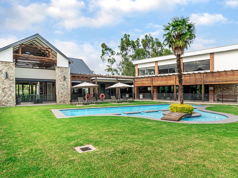 A well-maintained communal pool area featuring stone-clad architecture, timber pergolas, and a landscaped garden setting.