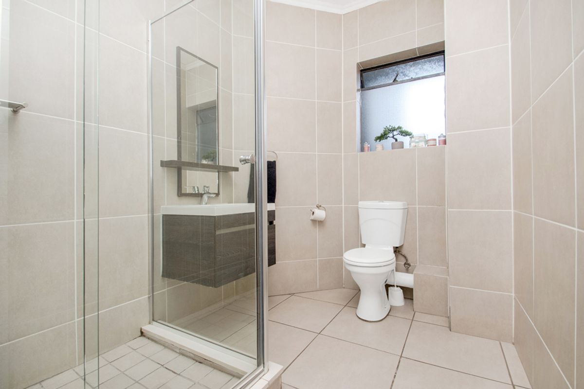 A clean, modern bathroom featuring a glass-enclosed shower, wall-mounted vanity, and neutral floor-to-ceiling tiling.