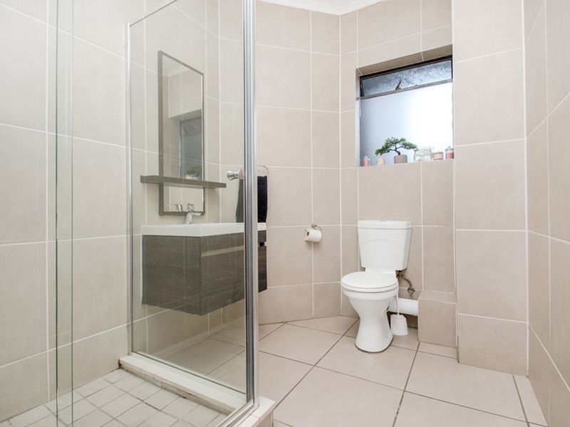 A clean, modern bathroom featuring a glass-enclosed shower, wall-mounted vanity, and neutral floor-to-ceiling tiling.