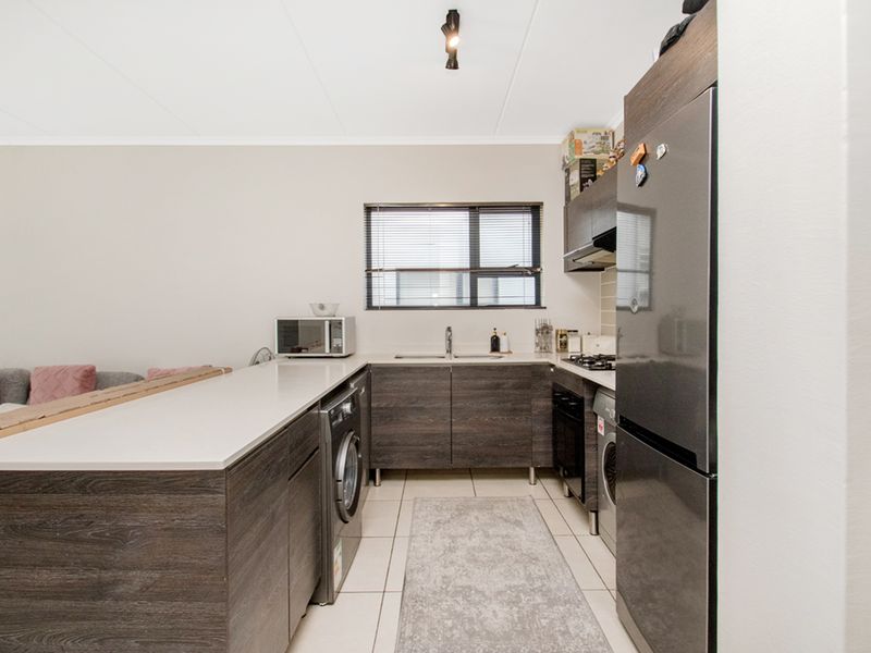 Modern kitchen featuring dark wood-grain cabinetry, stone countertops, integrated gas hob, extractor fan, and tiled flooring with a functional layout.