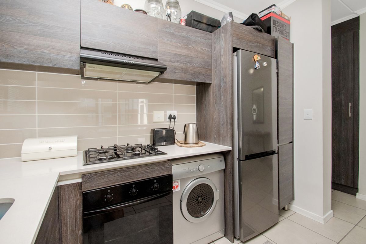 Modern kitchen featuring dark wood-grain cabinetry, stone countertops, a gas hob with extractor fan, and integrated laundry and refrigeration appliances.