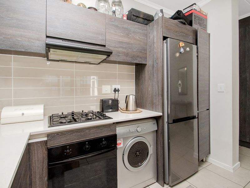 Modern kitchen featuring dark wood-grain cabinetry, stone countertops, a gas hob with extractor fan, and integrated laundry and refrigeration appliances.