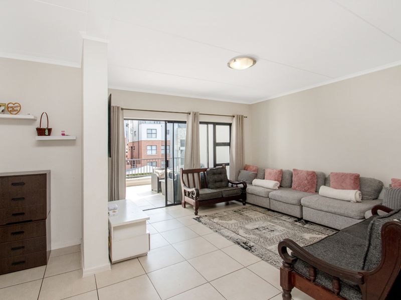 A bright and spacious living room featuring neutral tiled flooring and a large sliding glass door providing access to an outdoor balcony area.