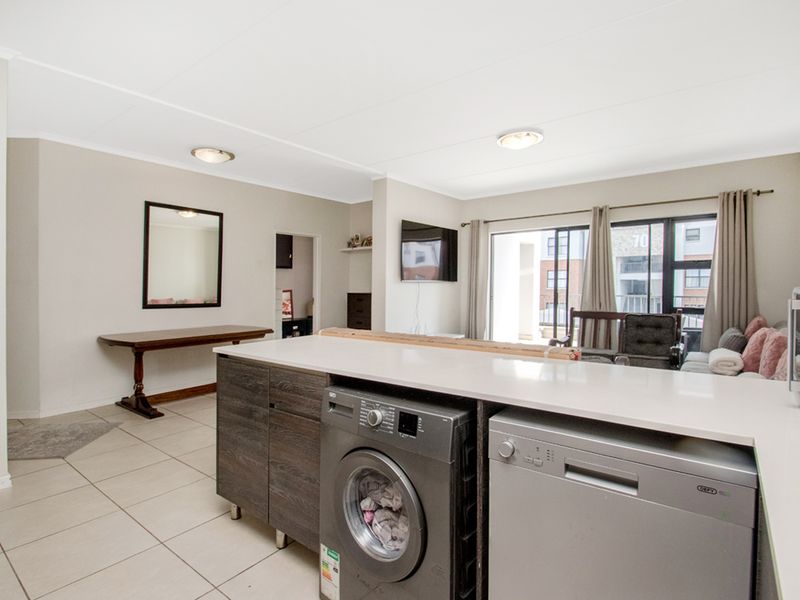 Open plan living area featuring a kitchen island with integrated appliance space, tiled flooring, and sliding glass doors leading to an outdoor balcony.