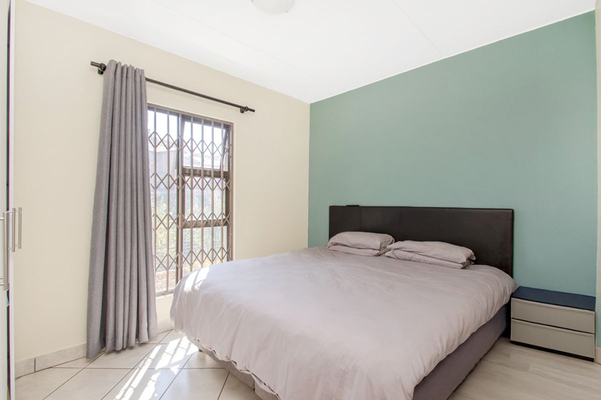 A well-lit bedroom featuring tiled flooring, a security gate on the window, and a built-in cupboard.