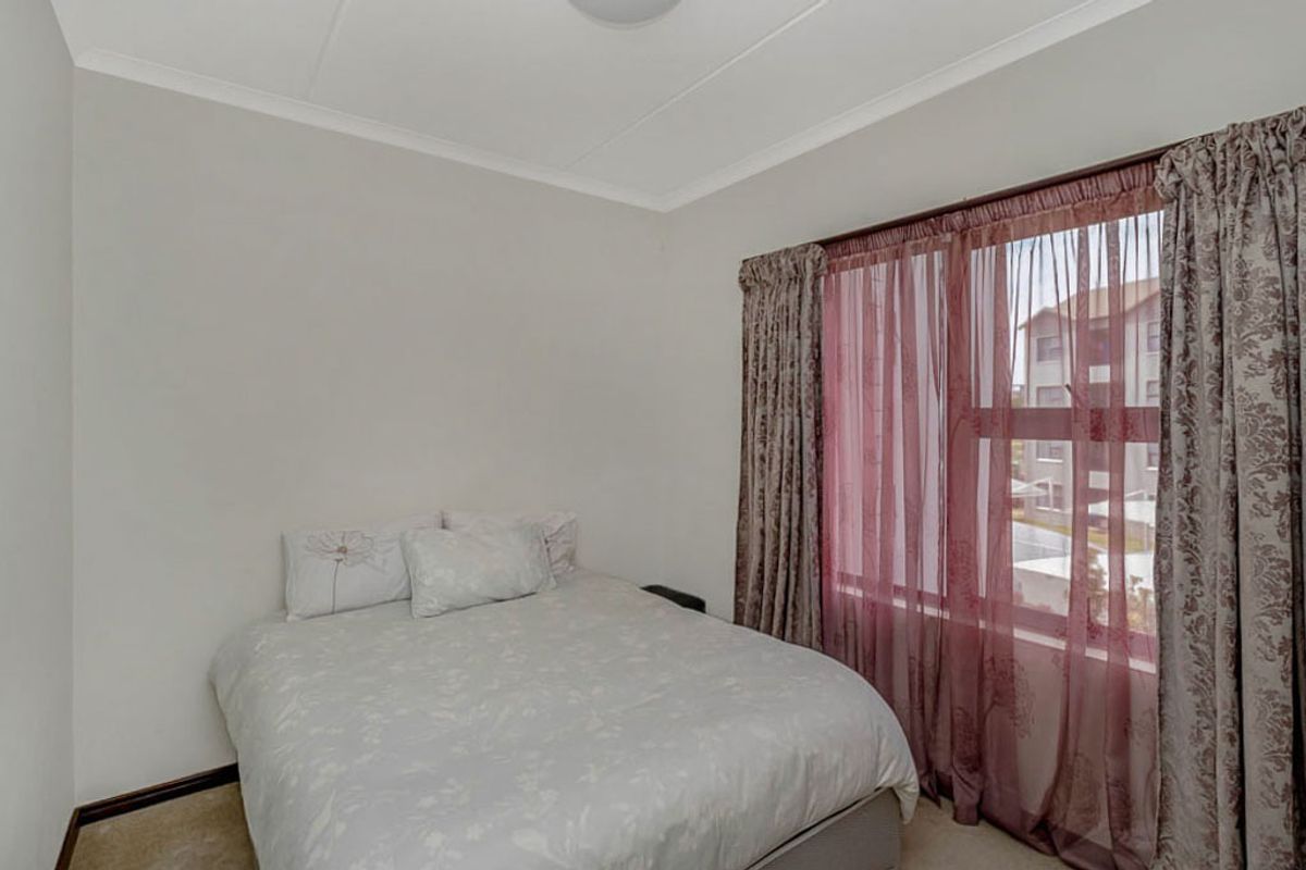 A standard bedroom featuring neutral walls, carpeted flooring, and a large window with curtain treatments.
