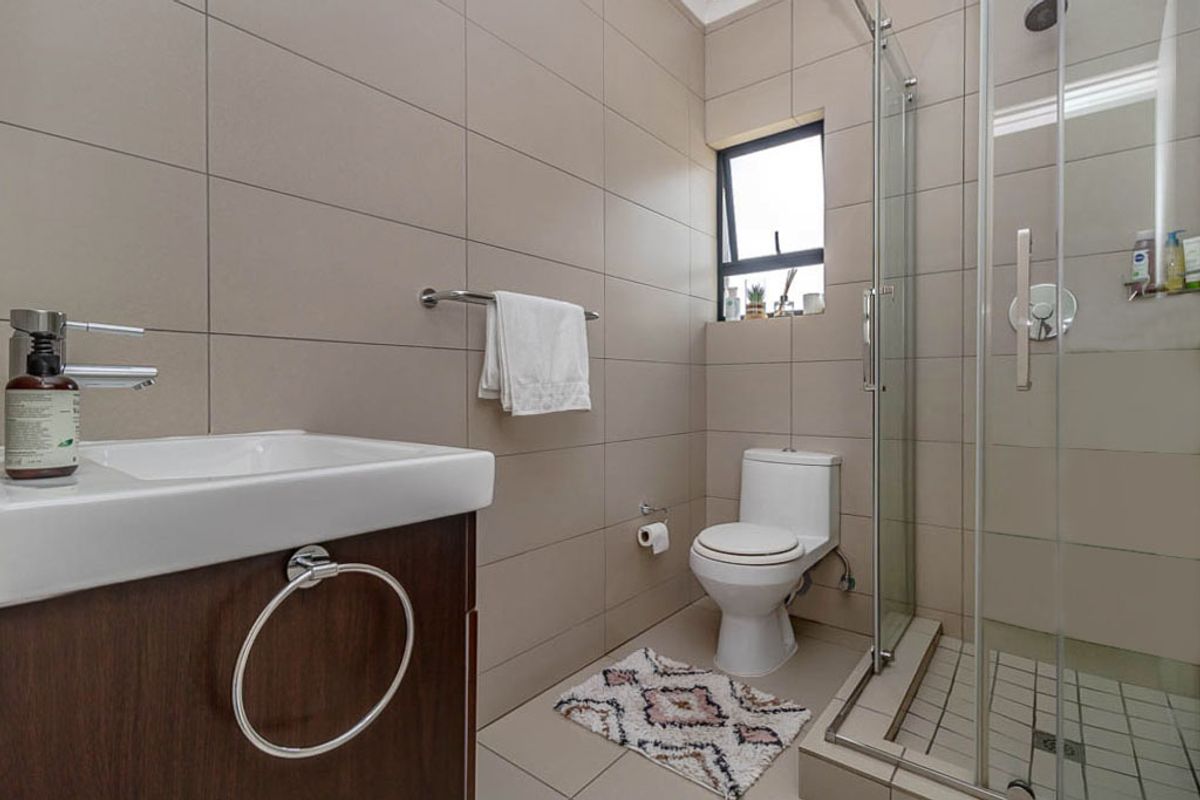 A modern bathroom featuring neutral wall tiles, a glass-enclosed shower, a vanity basin, and a toilet.