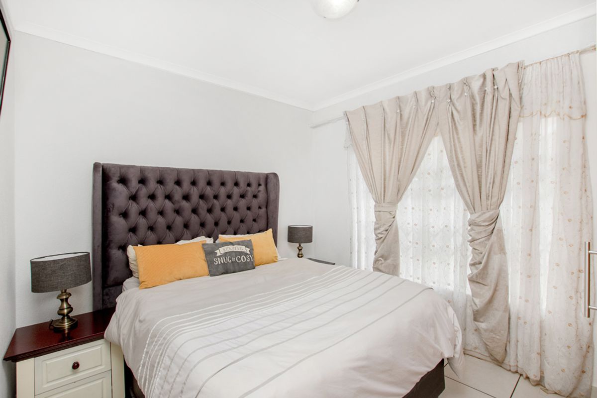 A well-lit bedroom featuring tiled flooring, neutral wall finishes, and a large window dressed with floor-to-ceiling curtains.