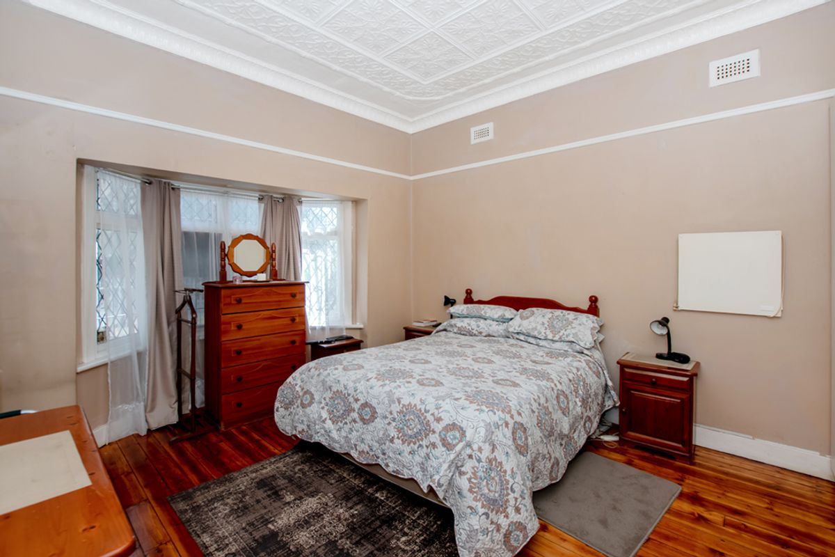 A bedroom featuring original pressed metal ceilings, timber flooring, and a bay window with leadlight detailing.