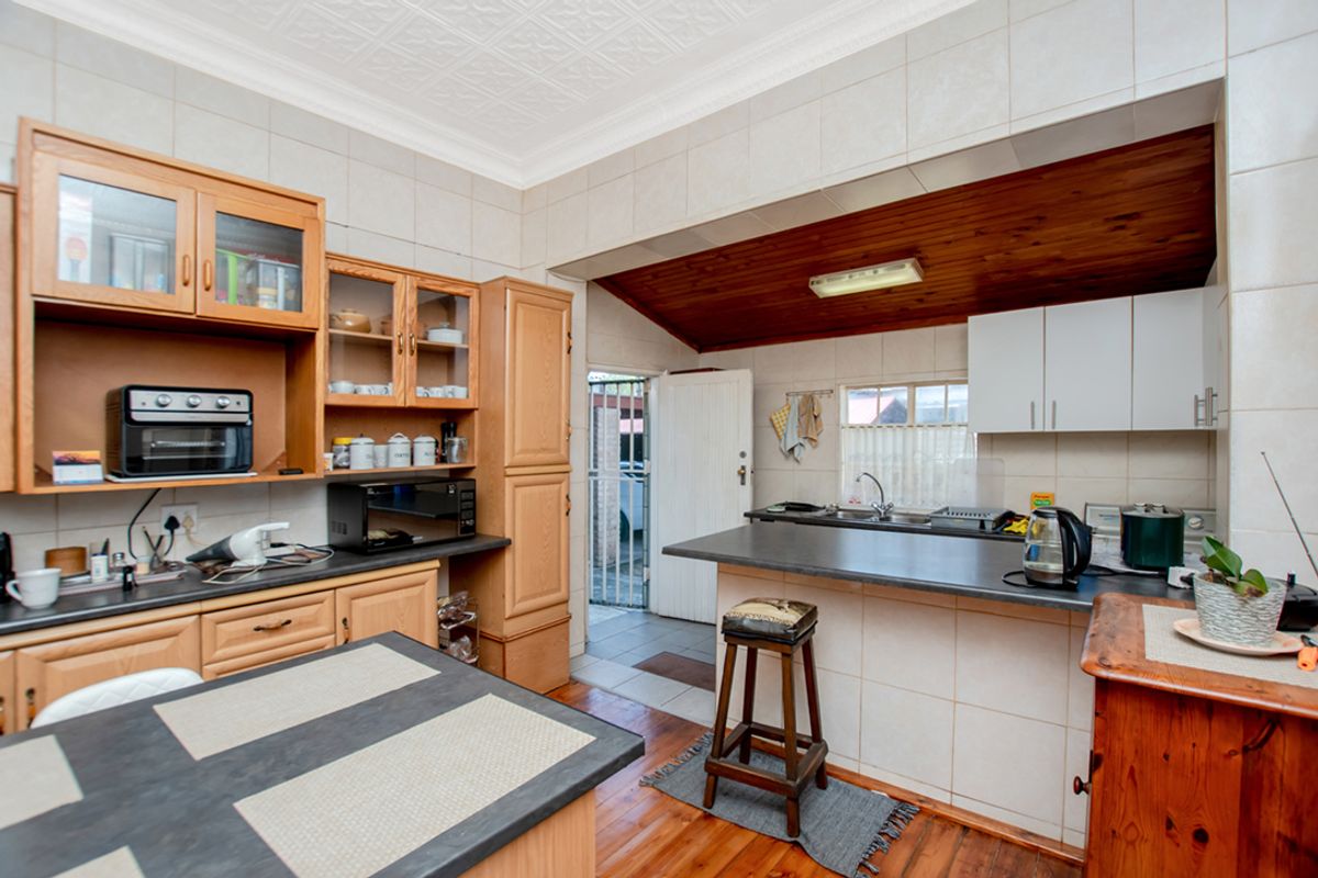 A functional kitchen featuring timber cabinetry, a breakfast bar, tiled splashbacks, and direct access to an exterior utility area.