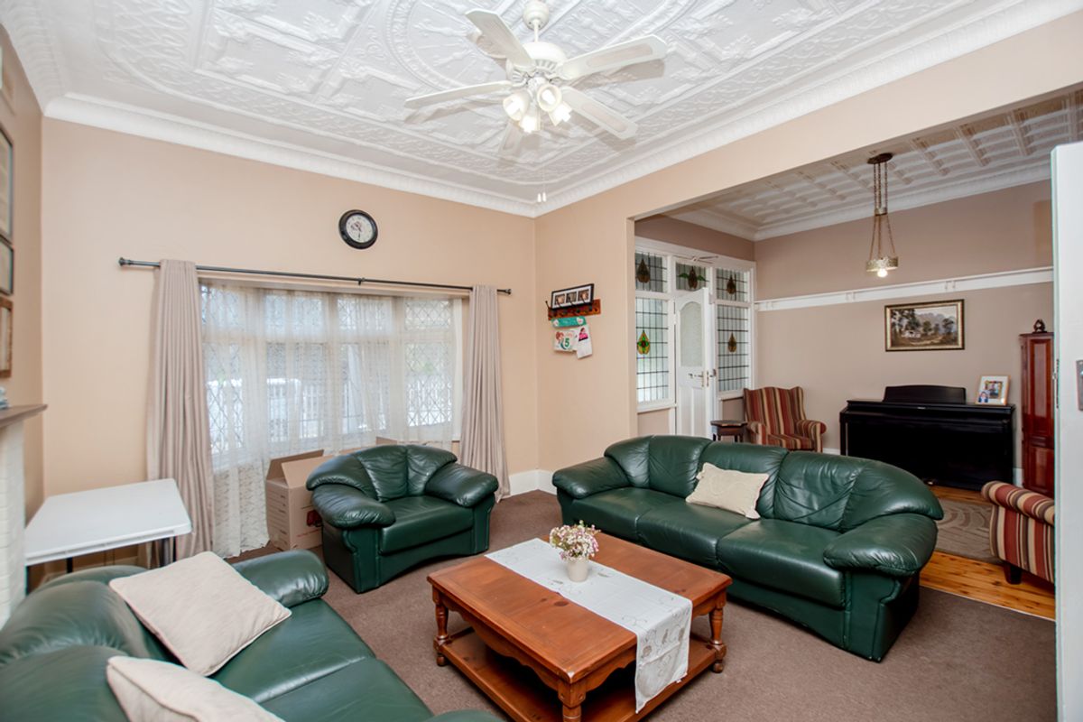 Spacious living room featuring ornate pressed metal ceilings, leadlight glass accents, and a large bay window, offering a classic architectural aesthetic.
