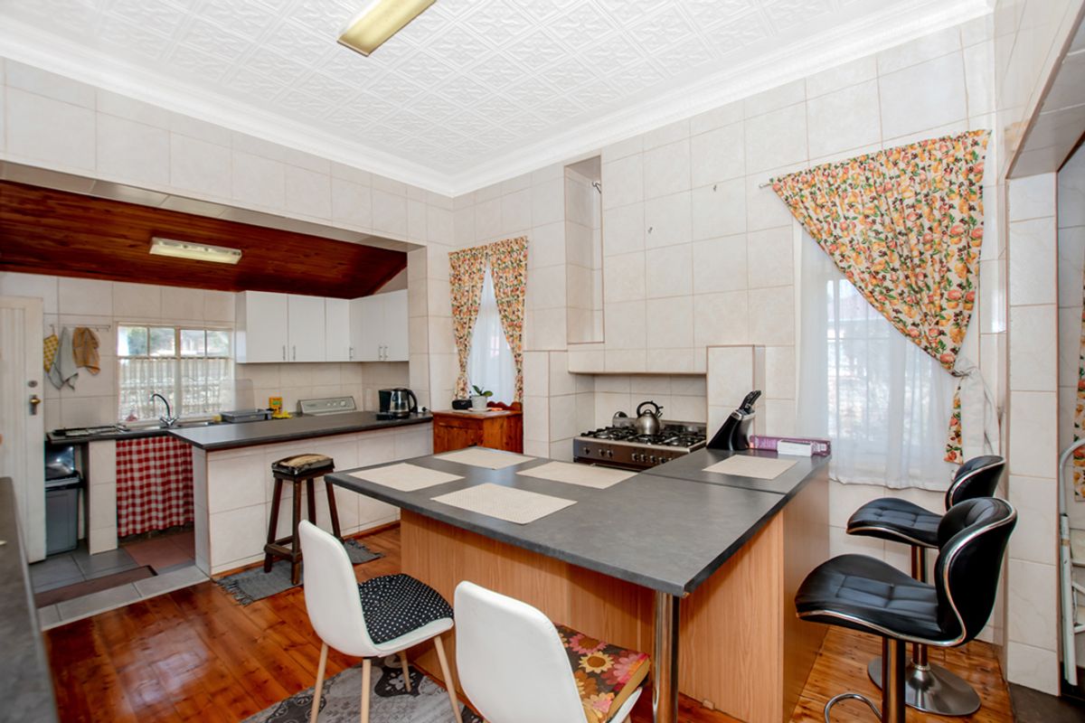 A functional kitchen featuring built-in cabinetry, a gas hob, oven, and tiled splashbacks, with a central breakfast bar and timber flooring.