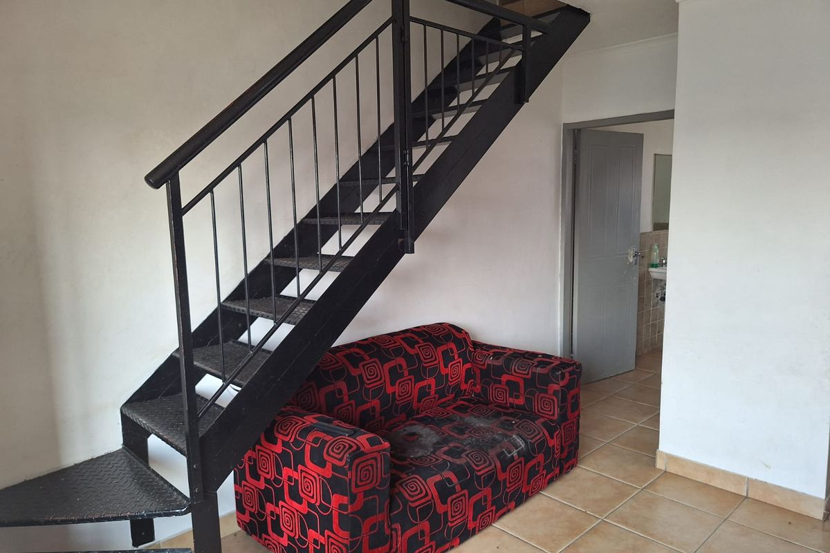 Living area featuring a metal staircase and tiled flooring, with direct access to an adjacent room.
