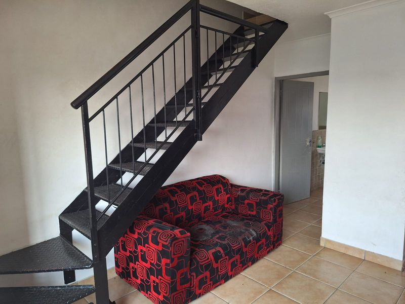 Living area featuring a metal staircase and tiled flooring, with direct access to an adjacent room.