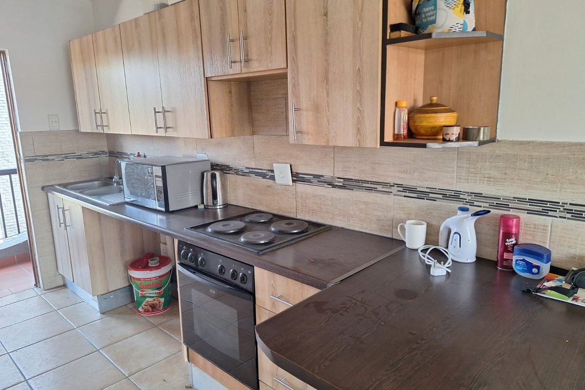 A functional kitchen featuring light wood-look cabinetry, dark laminate countertops, a built-in oven with electric hob, and neutral tiled flooring and backsplash.