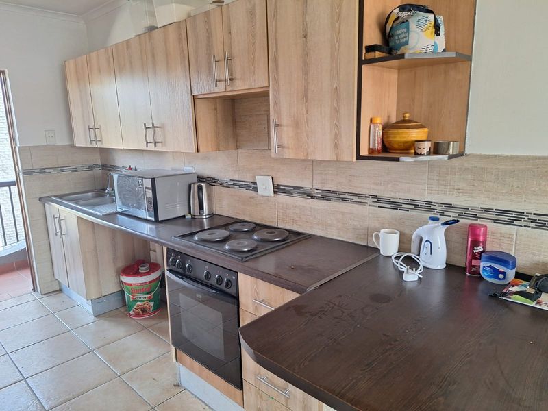 A functional kitchen featuring light wood-look cabinetry, dark laminate countertops, a built-in oven with electric hob, and neutral tiled flooring and backsplash.